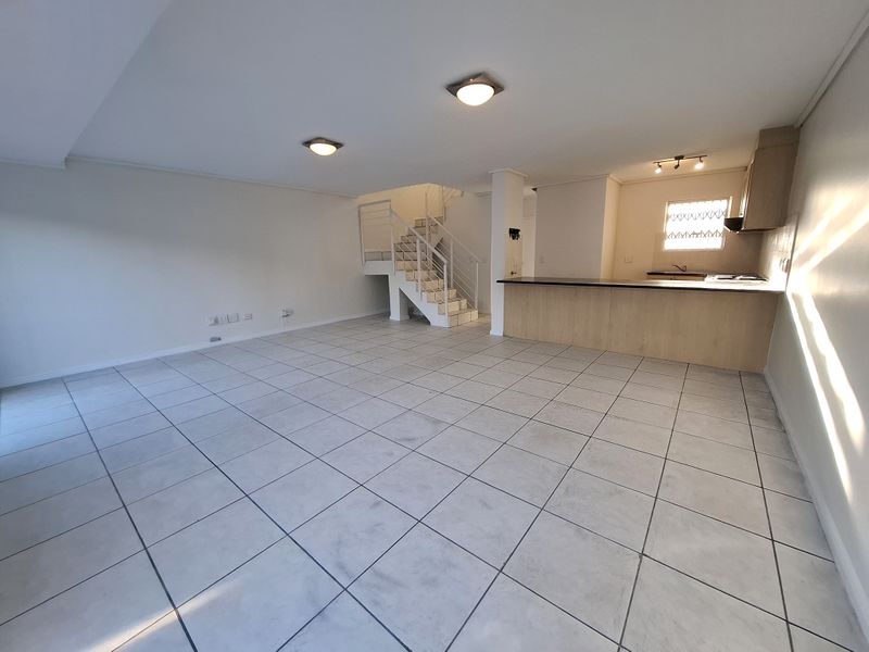 Spacious open-plan living area featuring tiled flooring, a central staircase, and a functional kitchen with a breakfast bar and built-in cabinetry.