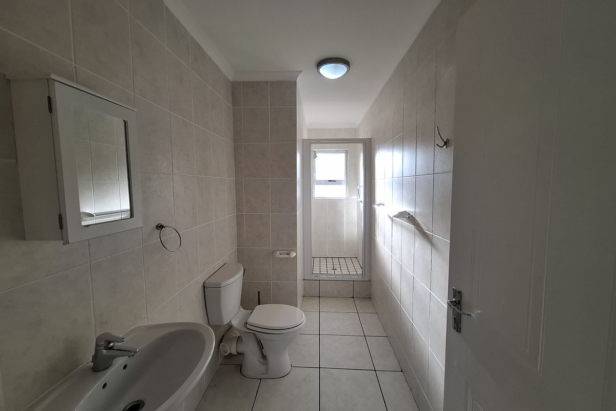 A functional bathroom featuring a pedestal basin, toilet, and a separate shower enclosure with tiled walls and flooring throughout.