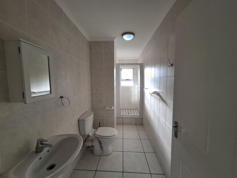 A functional bathroom featuring a pedestal basin, toilet, and a separate shower enclosure with tiled walls and flooring throughout.