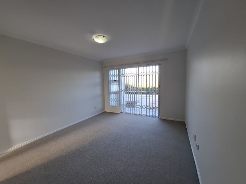 An empty, well-maintained bedroom featuring neutral carpeting, a ceiling light fixture, and a sliding glass door with an integrated security gate.
