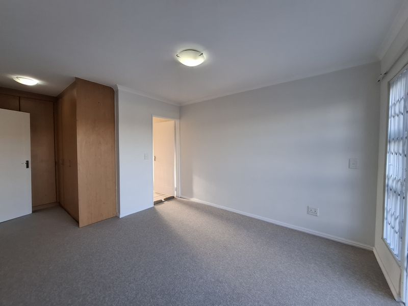 A clean, empty bedroom featuring neutral carpeting, built-in wooden cupboards, and a security gate on the window.