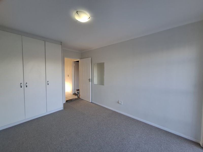 A clean, empty bedroom featuring neutral carpeting, built-in cupboards, and a wall-mounted mirror, offering a blank canvas for personalization.