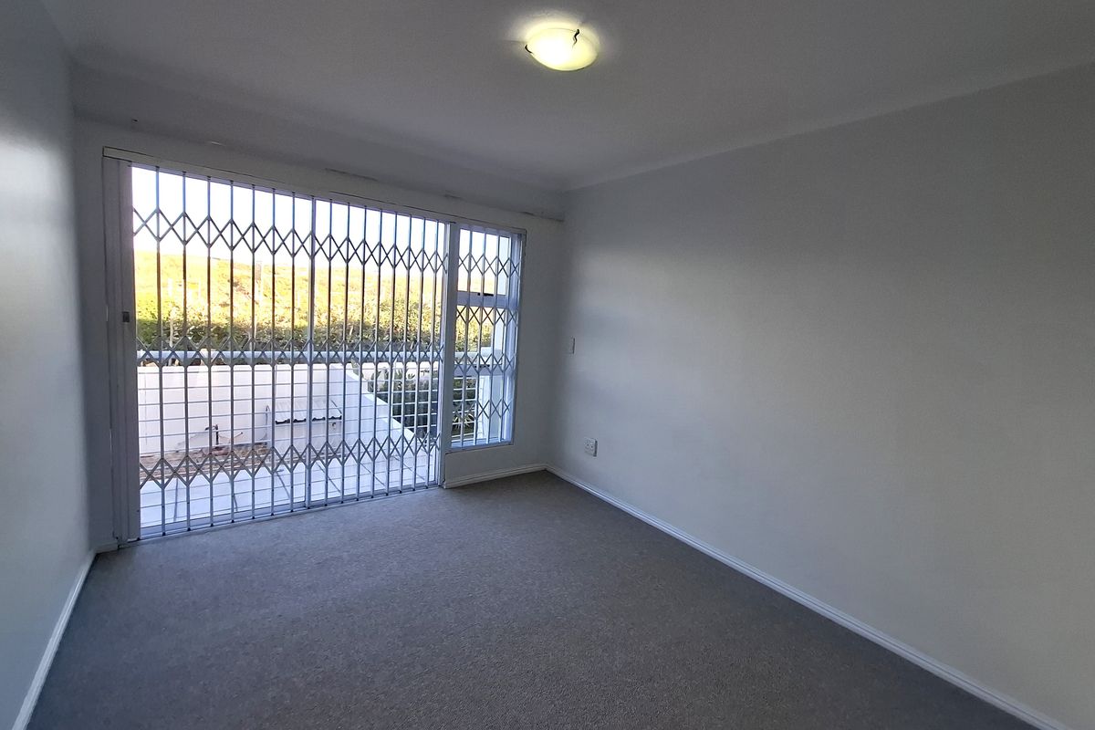 An empty bedroom featuring neutral carpeting, a ceiling light fixture, and a large window secured with a metal security gate.