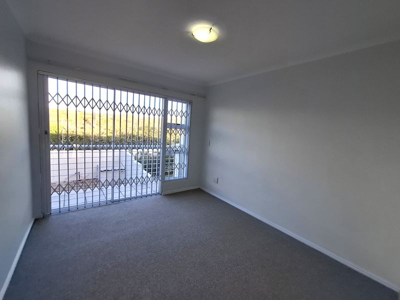 An empty bedroom featuring neutral carpeting, a ceiling light fixture, and a large window secured with a metal security gate.