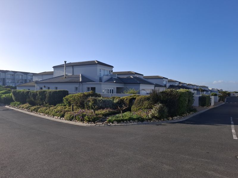A view of the townhouse complex exterior featuring a tiled roof, balcony, and well-maintained landscaped garden area from the street.