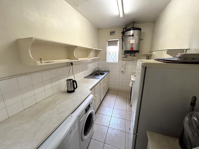 Functional laundry area featuring built-in cabinetry, a stainless steel sink, tiled backsplash, and an exposed electric water heater.