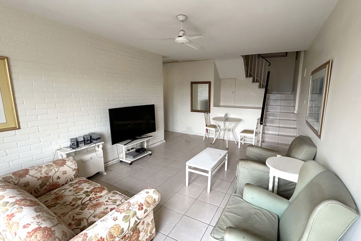 A living room featuring tiled flooring, a painted brick feature wall, and an integrated staircase leading to the upper level.
