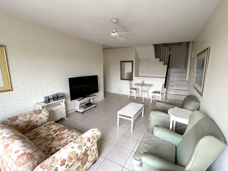 A living room featuring tiled flooring, a painted brick feature wall, and an integrated staircase leading to the upper level.