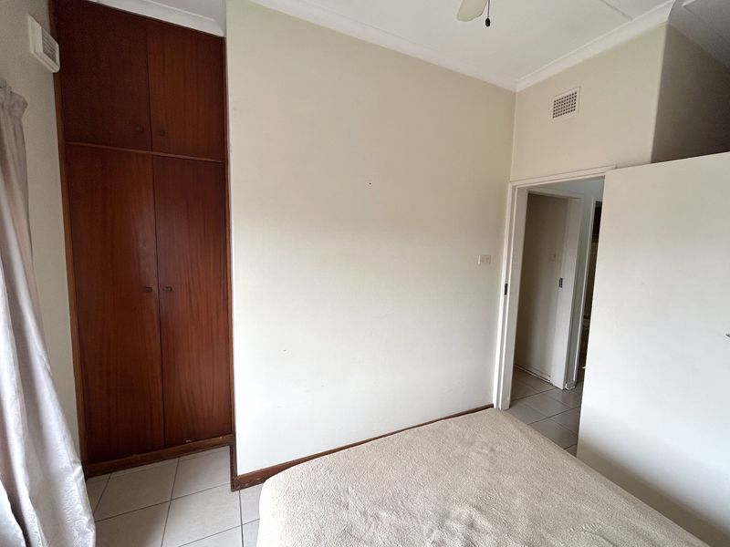 A bedroom featuring tiled flooring, a built-in wooden wardrobe, and a ceiling fan, offering a functional space ready for cosmetic updates.