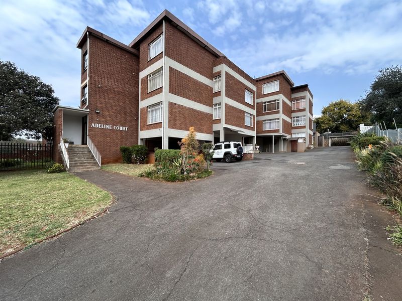 Exterior view of Adeline Court apartment building featuring a brick facade, concrete entrance stairs, and an asphalt driveway.