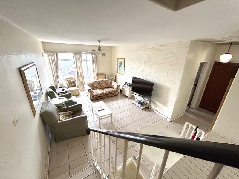 Spacious living area featuring a brick feature wall, tiled flooring, and a ceiling fan, viewed from the adjacent staircase.