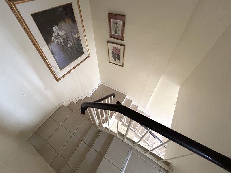 A view looking down a tiled staircase featuring a metal balustrade and handrail, showing a functional but dated interior transition space.