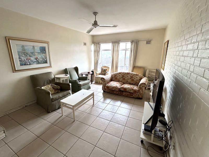 A living room featuring tiled flooring, a ceiling fan, and a painted brick feature wall, offering a functional space with potential for modernization.