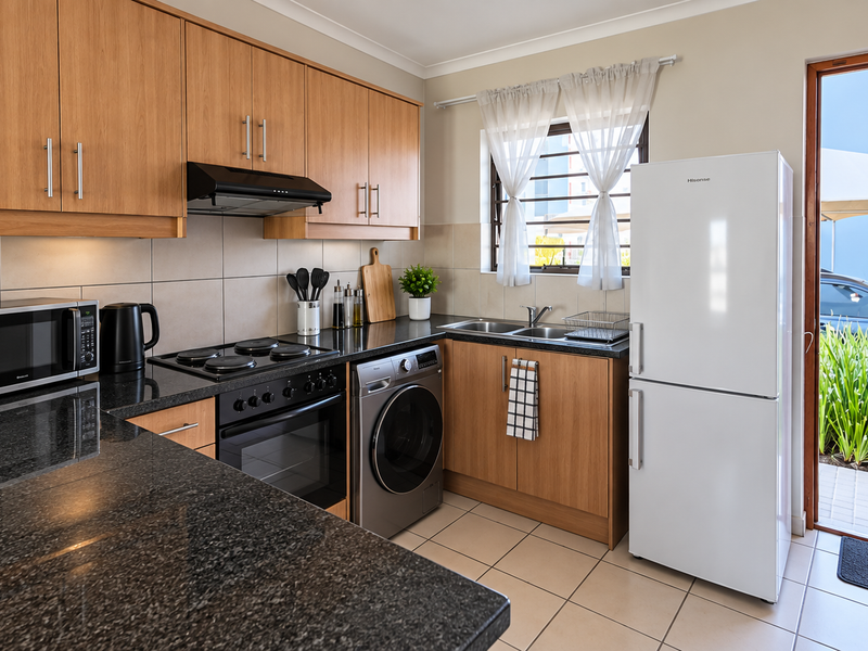 A well-maintained kitchen featuring wood-finish cabinetry, granite countertops, integrated appliances, and direct access to an outdoor area through a security gate.