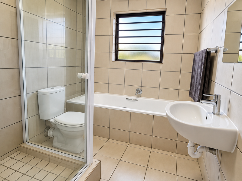 A clean, modern bathroom featuring a glass-enclosed shower, a built-in bathtub, and a wall-mounted basin with neutral floor-to-ceiling tiling.
