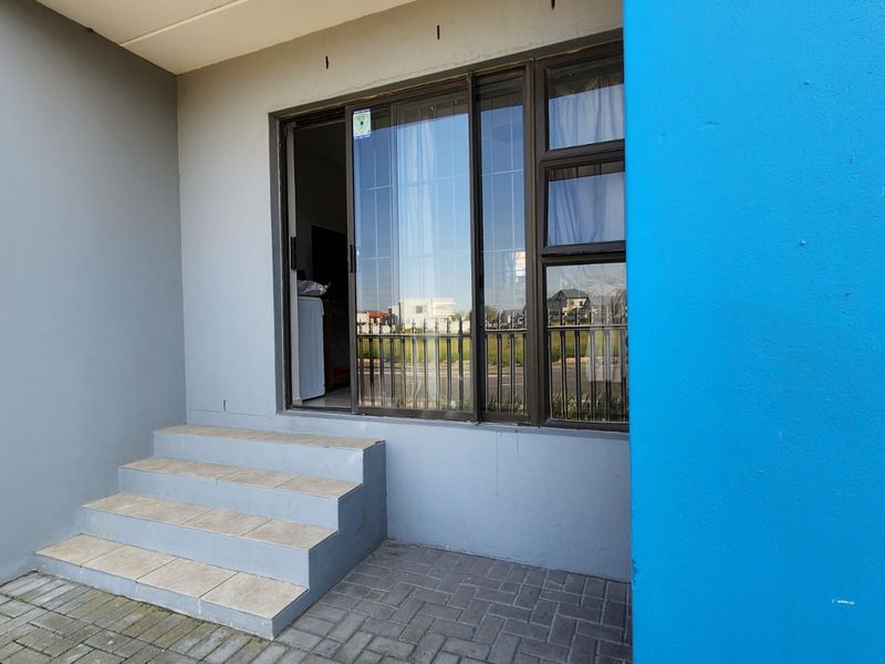 A paved patio area featuring tiled steps leading to a sliding glass door entrance with a modern grey and blue exterior finish.