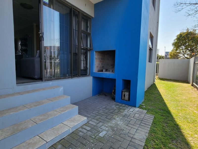 Outdoor patio area featuring a built-in braai, paved flooring, and tiled steps leading to a sliding glass door entrance.