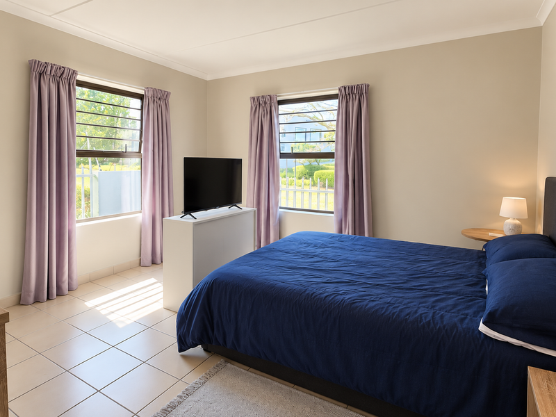 A well-lit bedroom featuring neutral wall tones, tiled flooring, and two windows equipped with security bars.