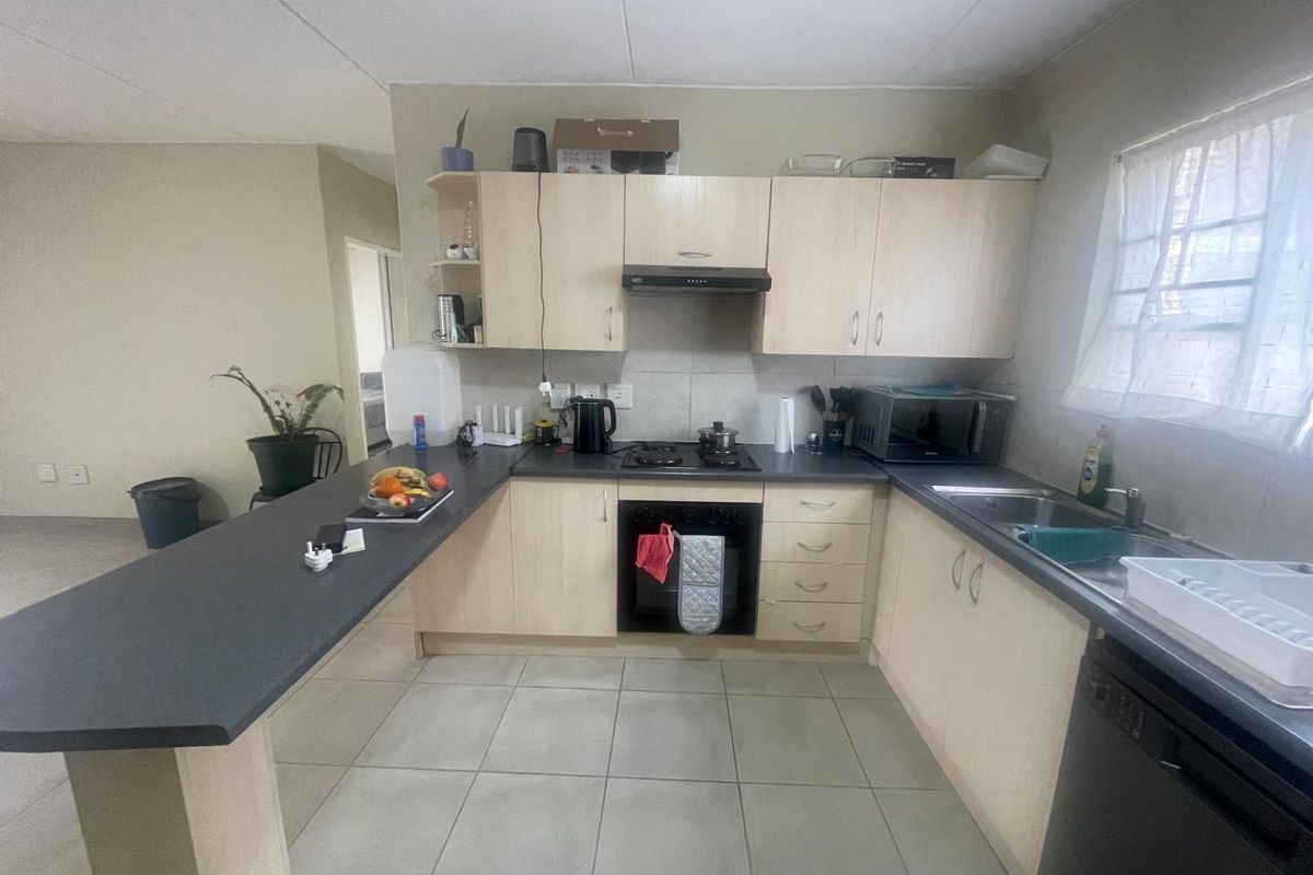 A functional kitchen featuring light wood cabinetry, dark laminate countertops, a breakfast bar, built-in oven, gas hob, and tiled flooring.