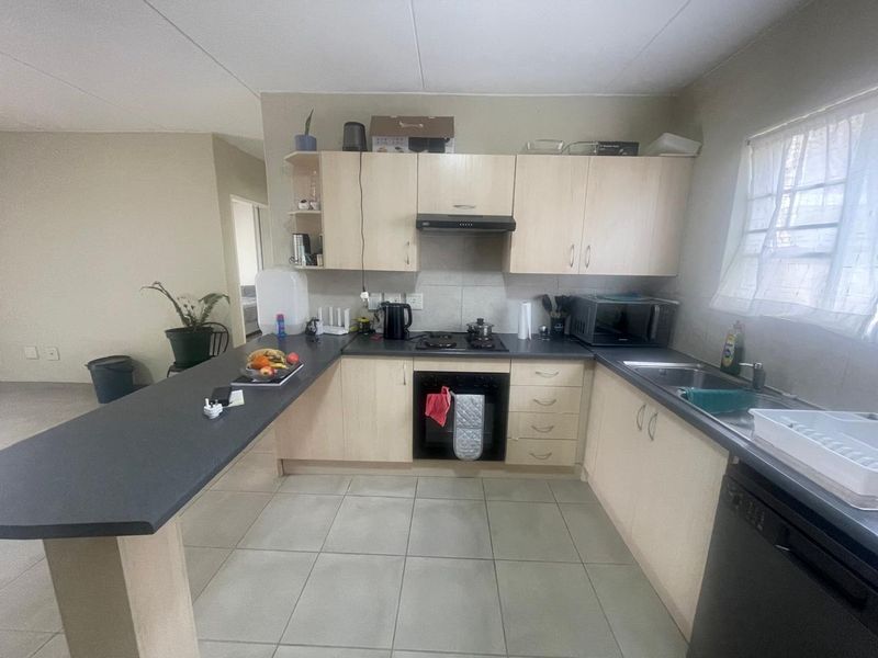 A functional kitchen featuring light wood cabinetry, dark laminate countertops, a breakfast bar, built-in oven, gas hob, and tiled flooring.
