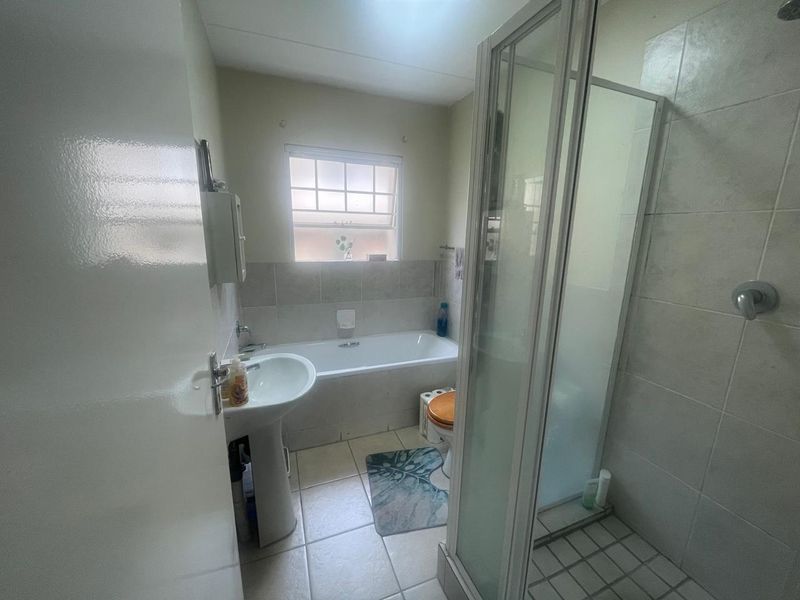 A functional bathroom featuring a pedestal basin, a built-in bathtub, and a separate shower enclosure with tiled finishes throughout.