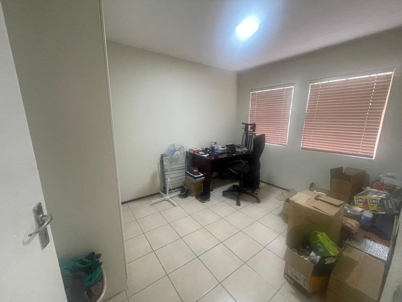 A functional bedroom space featuring tiled flooring, built-in storage, and venetian blinds, offering a neutral canvas for potential updates or staging.