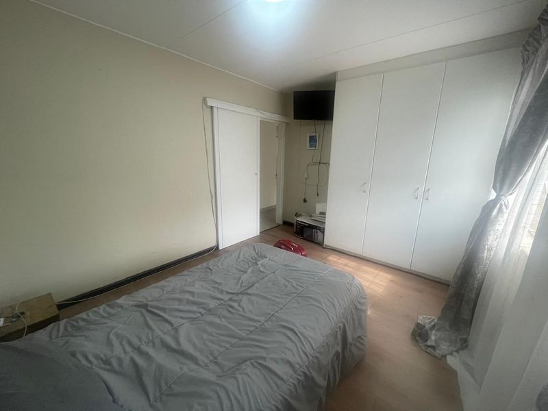 A functional bedroom featuring built-in cupboards, laminate flooring, and a sliding door entrance, offering a neutral space ready for personalization.