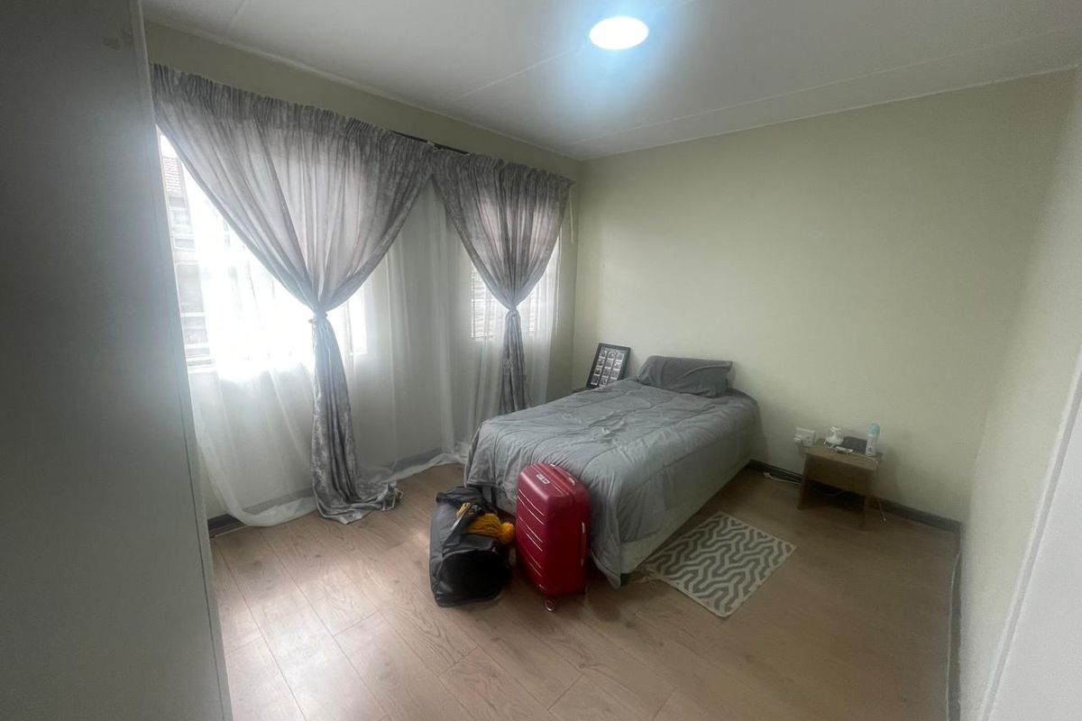 A bedroom featuring light-toned laminate flooring, neutral walls, and large windows with installed curtain tracks.