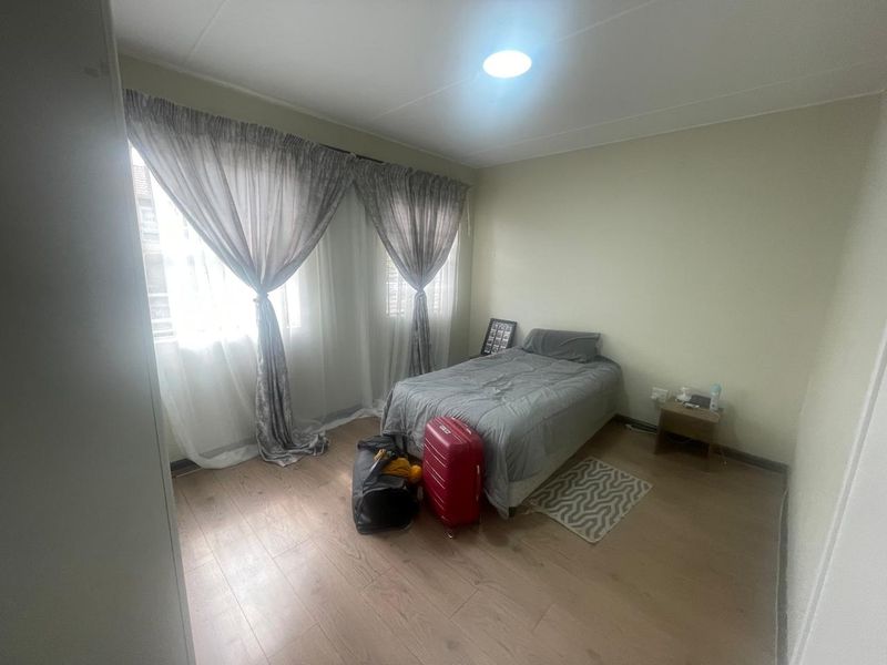 A bedroom featuring light-toned laminate flooring, neutral walls, and large windows with installed curtain tracks.