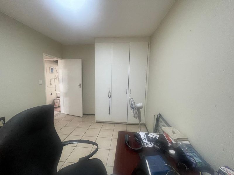 A bedroom featuring built-in cupboards and tiled flooring, currently used as a home office space.