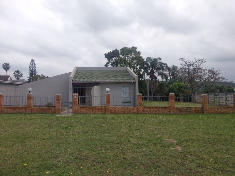 Front view of a single-story house featuring a brick boundary wall, metal fencing, and a tiled roof set on a spacious lawn.