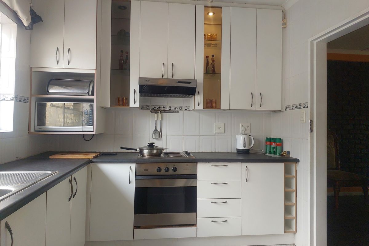 A functional kitchen featuring white cabinetry, dark laminate countertops, built-in oven, electric hob, and tiled backsplash with neutral floor tiles.
