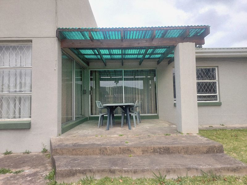 A covered rear patio featuring a corrugated roof, concrete flooring, and sliding glass door access to the main house.
