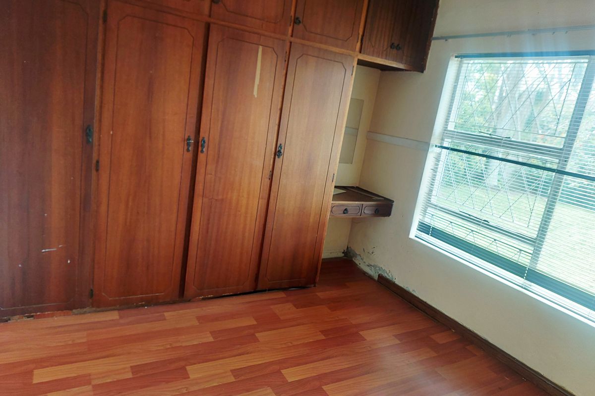 A bedroom featuring built-in wooden cupboards, a small integrated vanity desk, laminate flooring, and a window with security bars.