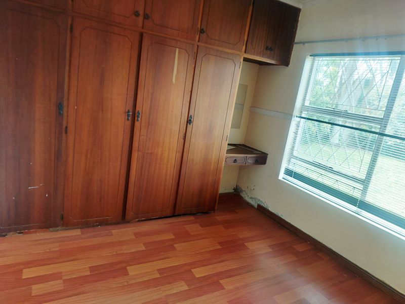 A bedroom featuring built-in wooden cupboards, a small integrated vanity desk, laminate flooring, and a window with security bars.