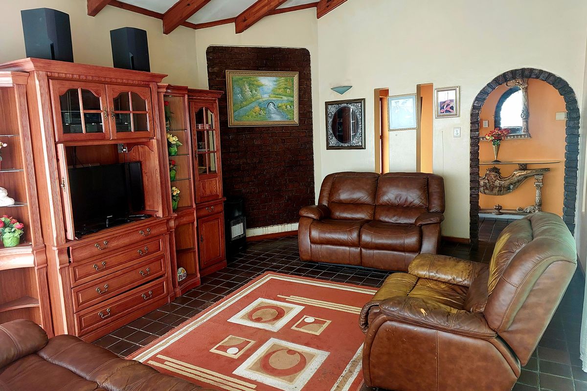Living room featuring exposed timber ceiling beams, a brick feature wall, and tiled flooring with an arched entryway leading to adjacent spaces.