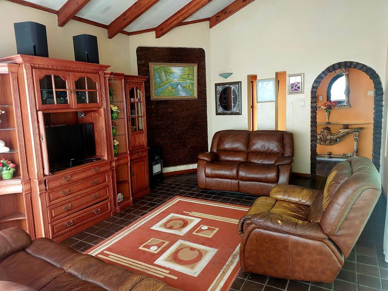 Living room featuring exposed timber ceiling beams, a brick feature wall, and tiled flooring with an arched entryway leading to adjacent spaces.
