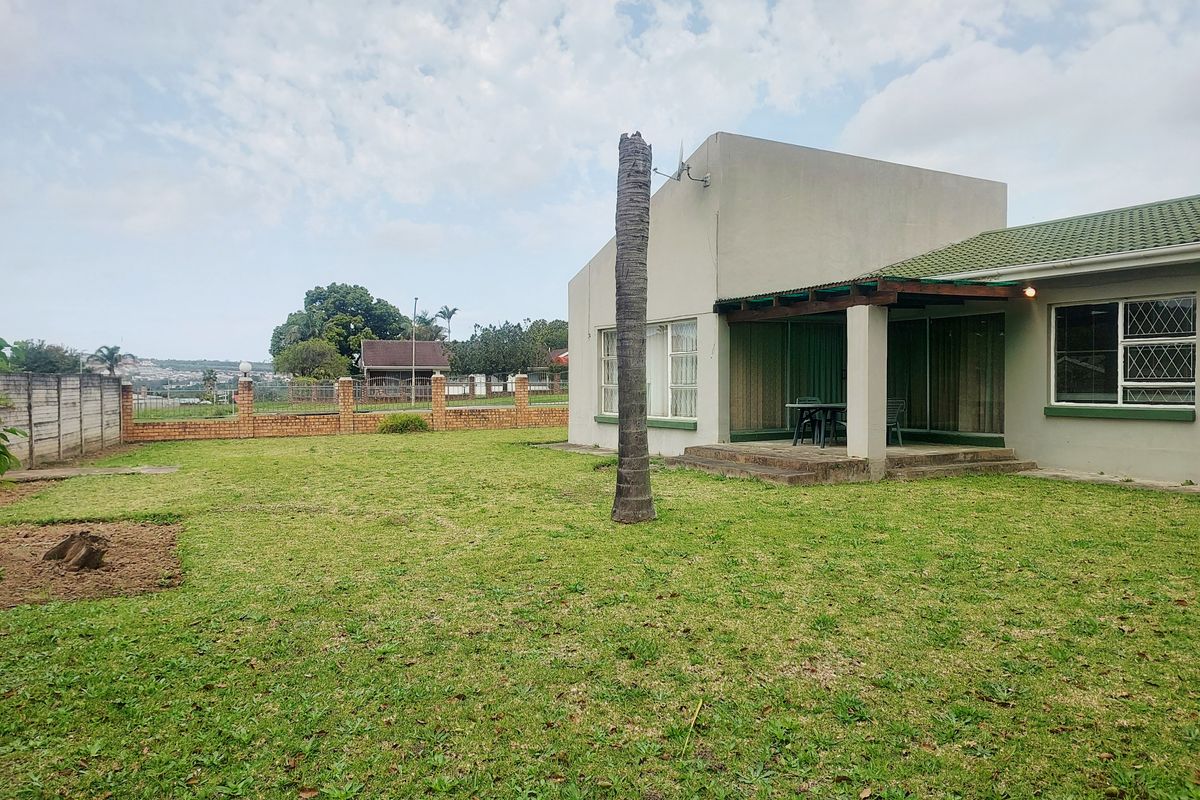 Rear view of the property featuring a covered patio, a spacious lawn, and a brick boundary wall.