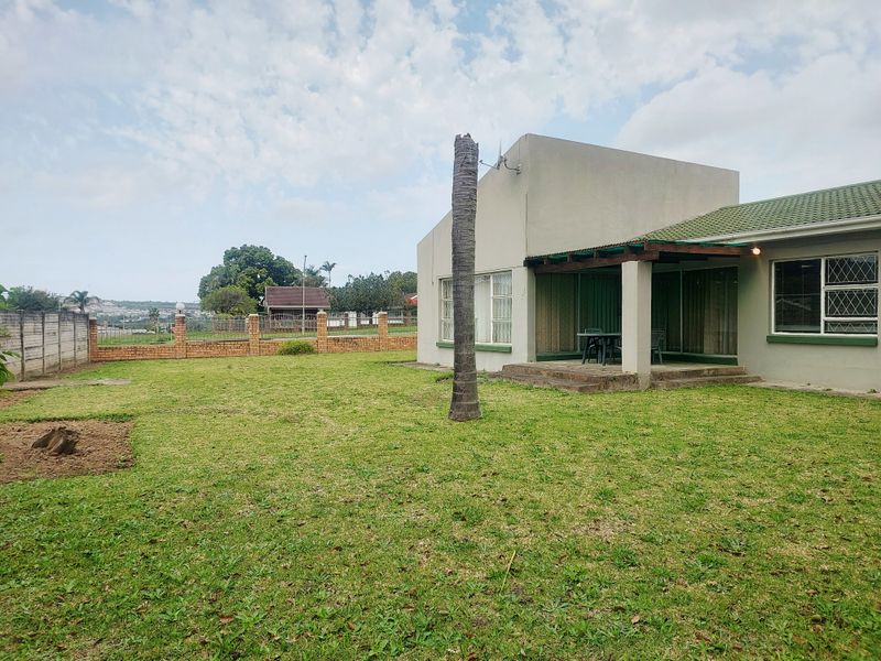 Rear view of the property featuring a covered patio, a spacious lawn, and a brick boundary wall.