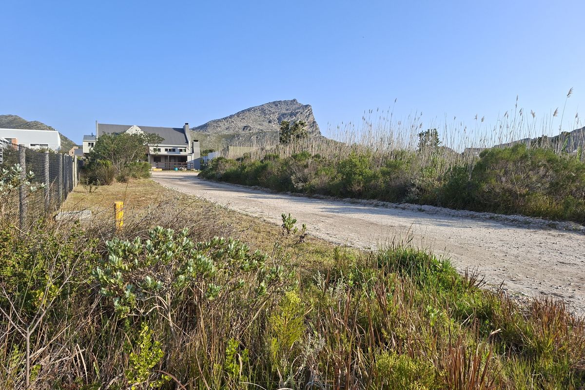 A view of an unpaved access road leading towards a residential property, surrounded by natural vegetation and mountain views.