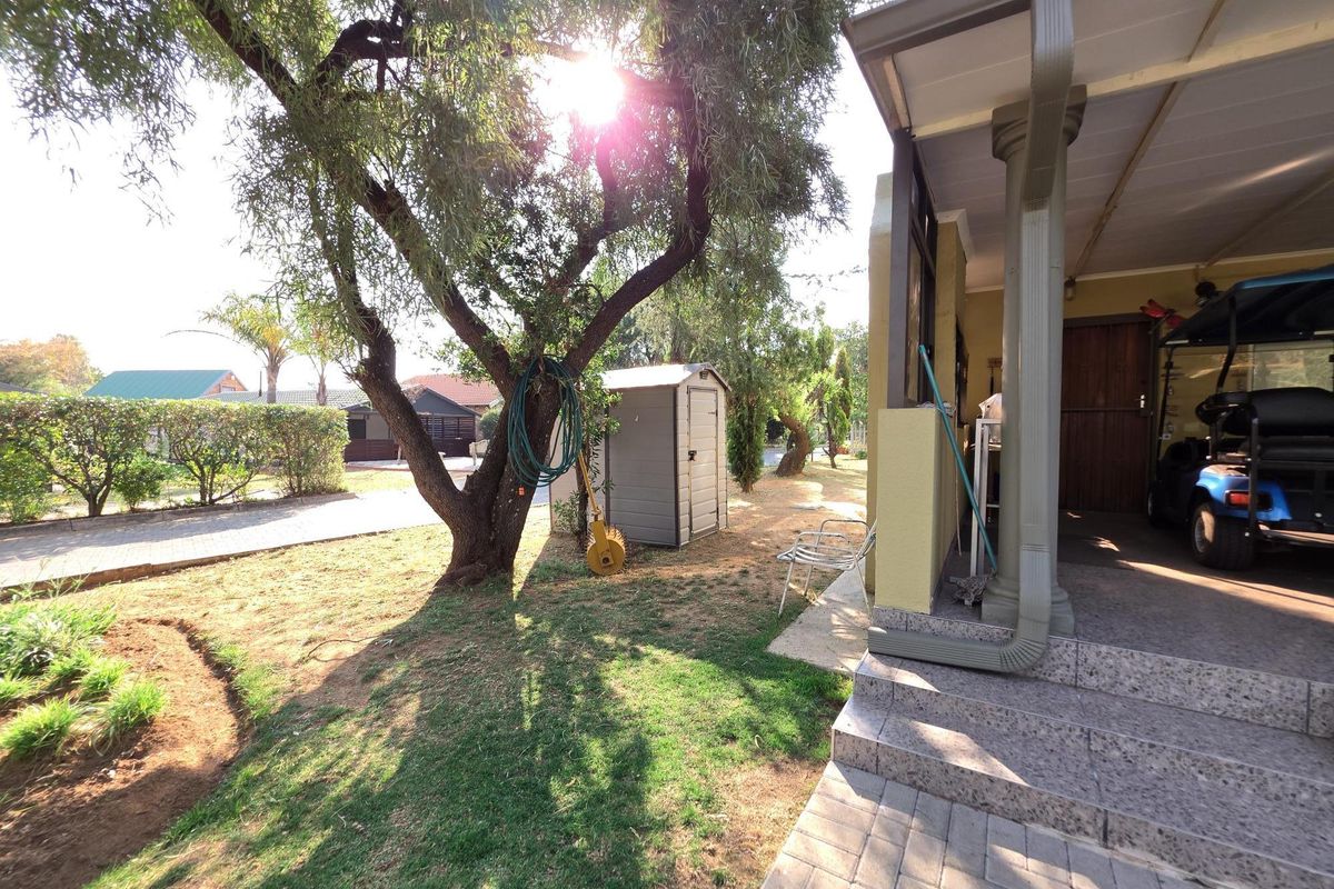 A view of the rear garden featuring a covered patio with stone steps, a paved driveway, and mature trees.
