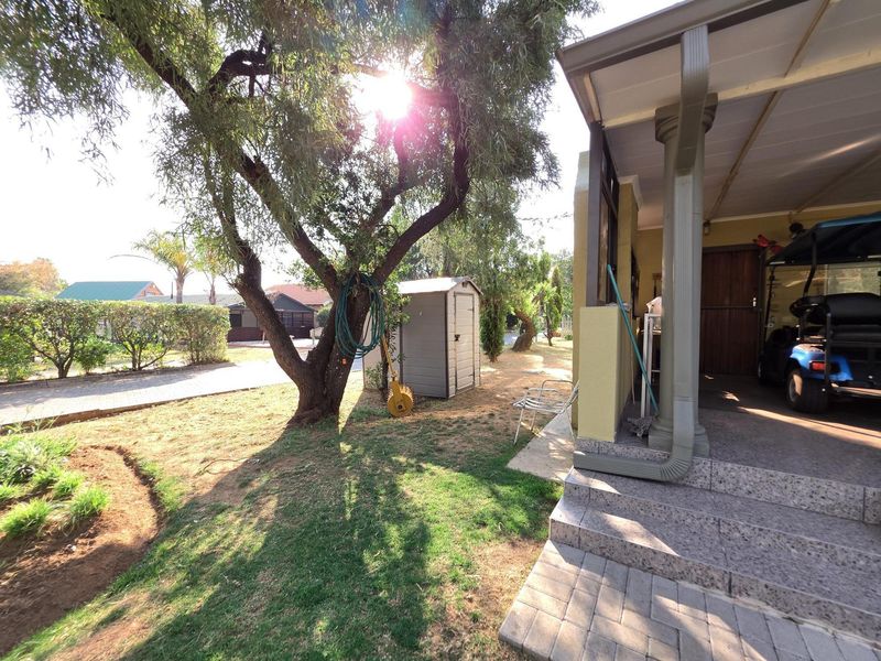 A view of the rear garden featuring a covered patio with stone steps, a paved driveway, and mature trees.