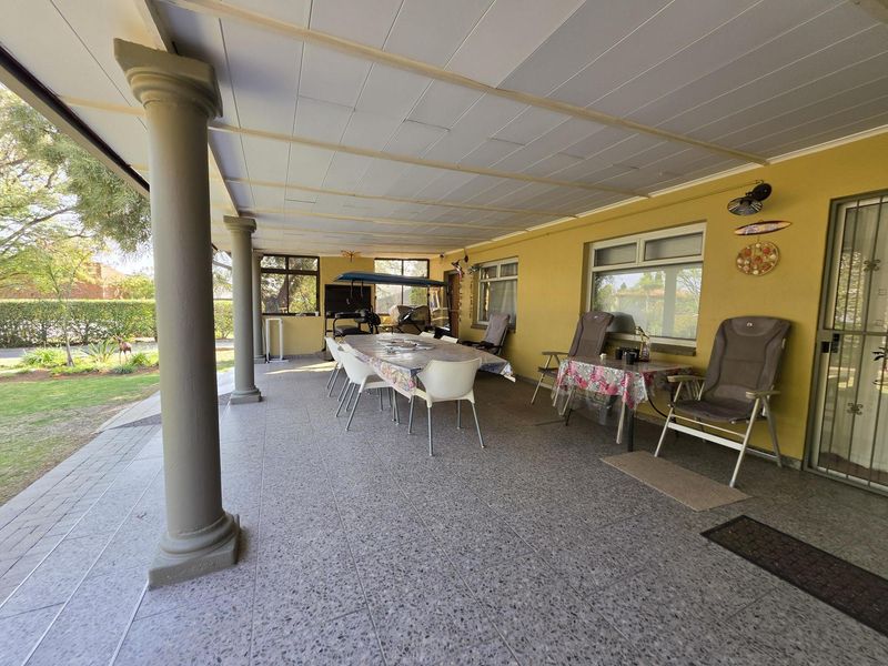 A spacious covered patio featuring terrazzo flooring and structural columns, providing an ideal outdoor entertainment area overlooking the garden.