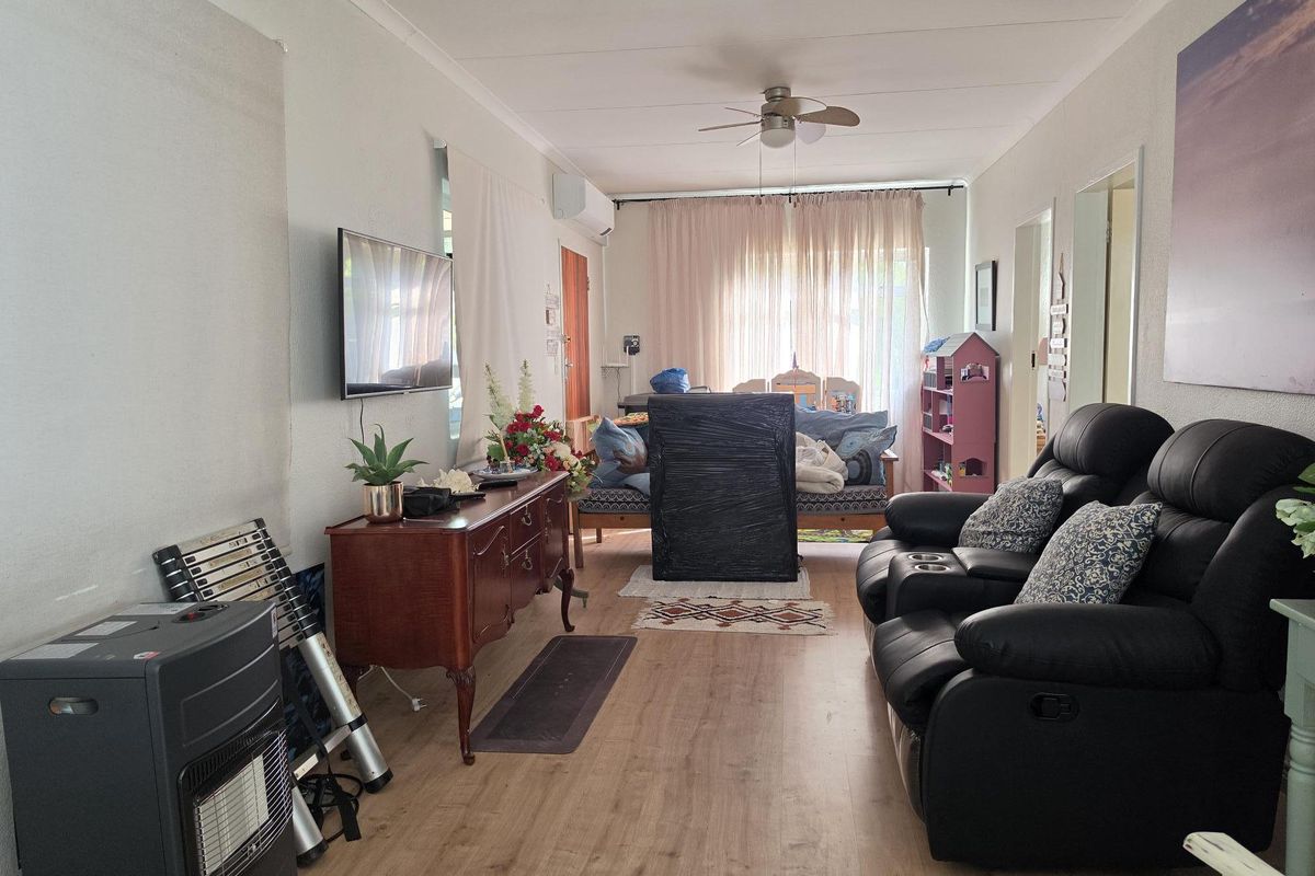 A living room featuring laminate flooring, a ceiling fan, and a wall-mounted air conditioning unit.