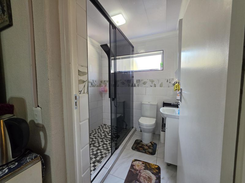 A functional bathroom featuring a modern glass-enclosed shower, a white pedestal sink, and a toilet, finished with clean wall and floor tiling.