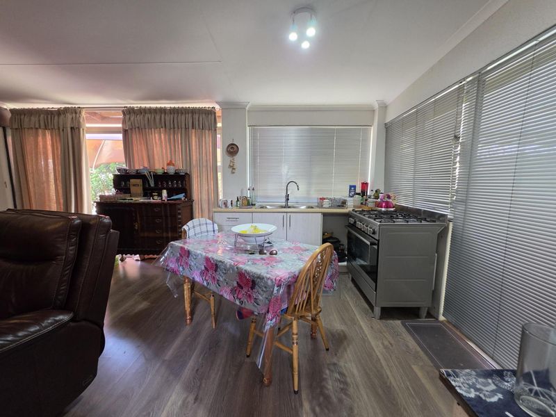 Open plan kitchen and dining area featuring laminate flooring, functional cabinetry, and a freestanding gas stove with large windows and venetian blinds.
