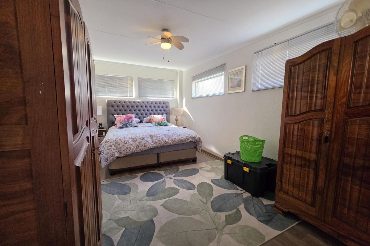 A well-lit bedroom featuring laminate flooring, a ceiling fan, and multiple windows with venetian blinds.