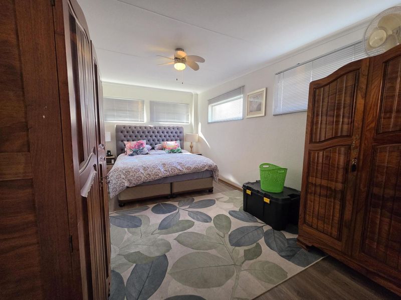 A well-lit bedroom featuring laminate flooring, a ceiling fan, and multiple windows with venetian blinds.