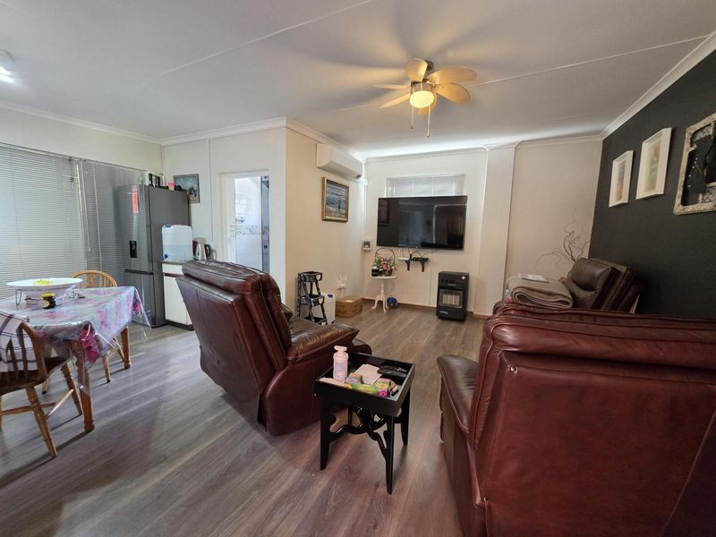 Open plan living and dining area featuring laminate flooring, a ceiling fan, and a wall-mounted split system air conditioner.