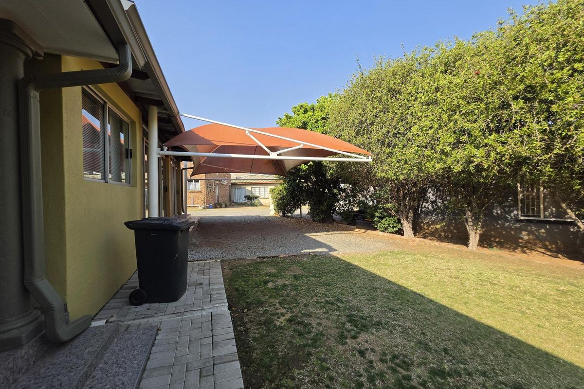 Rear exterior view featuring a gravel driveway, a shade sail structure, and a paved walkway alongside the house.